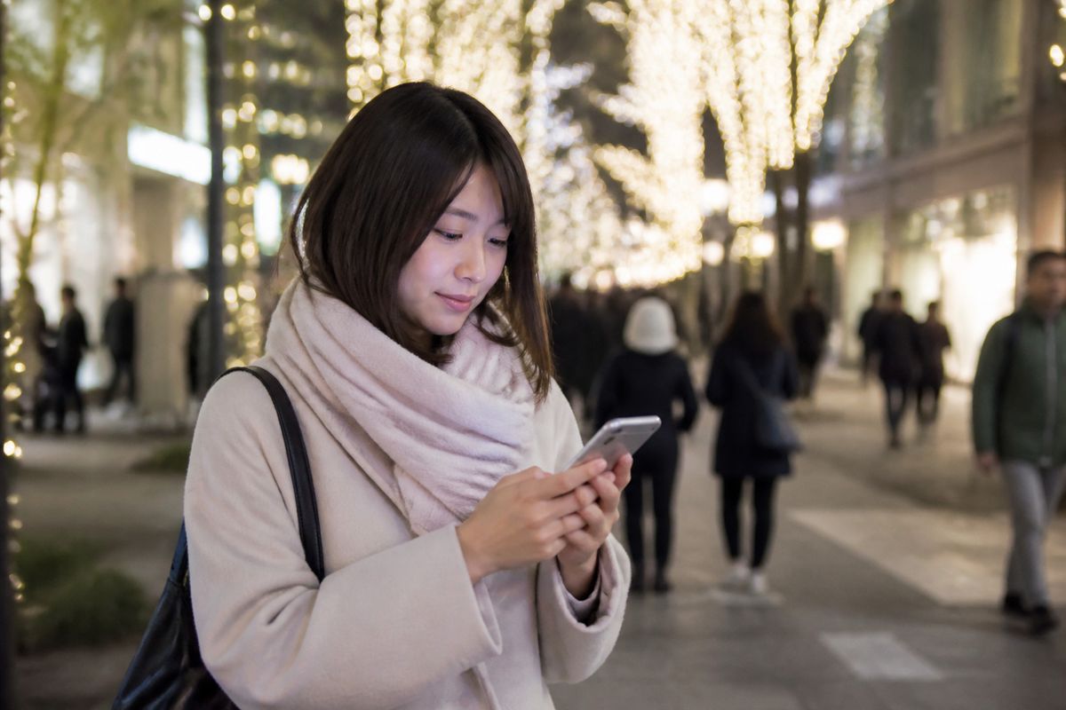 商店街のイルミネーションの下でスマホを操作する来街者