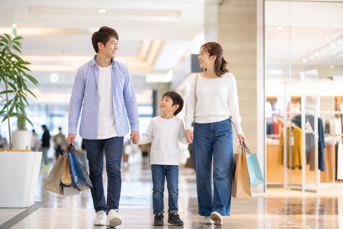 大型商業施設のフロアで買い物袋を提げながら歩く家族連れ