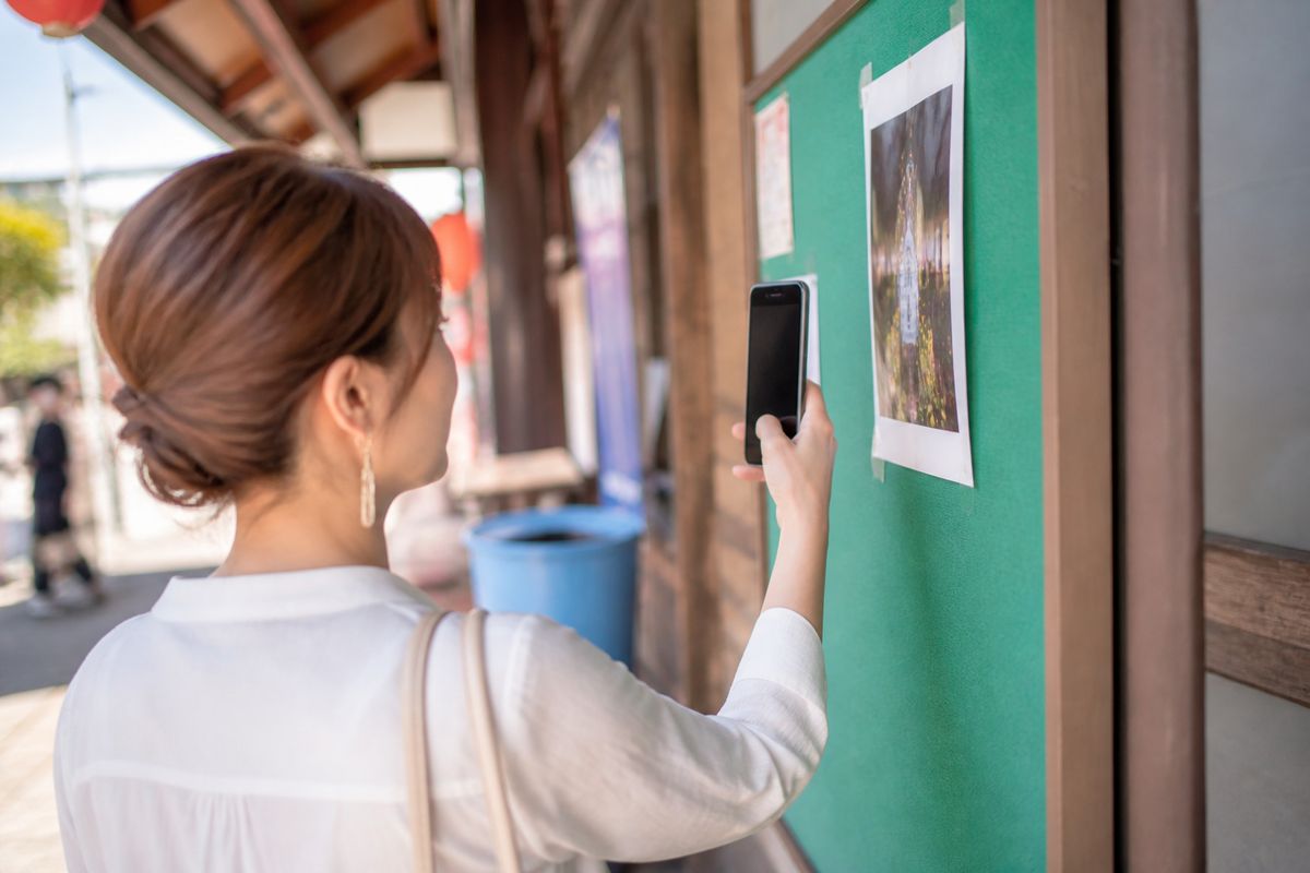 商店街の掲示物を確認しながらスマートフォンをかざす来場者
