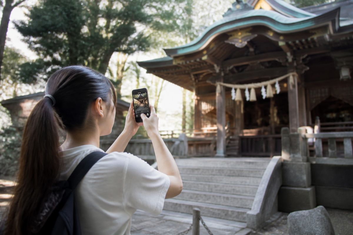 アニメの舞台となった神社の前でスマホを構える若いファン