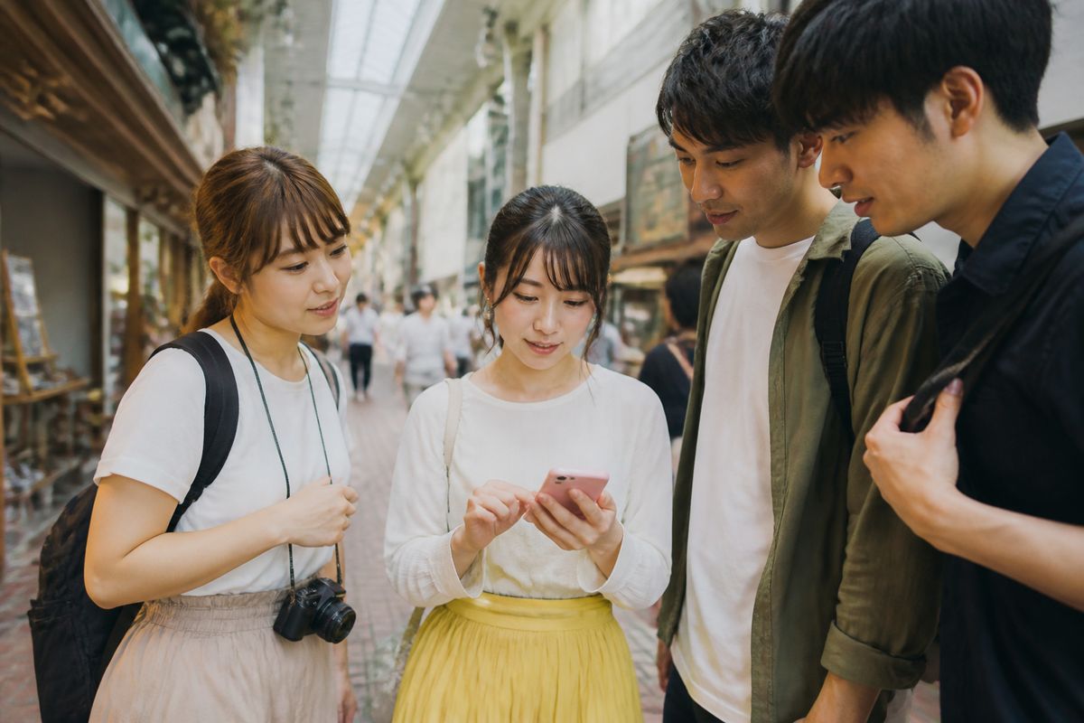 商店街のアーケードを歩きながらスマホで地図を確認する観光客のグループ
