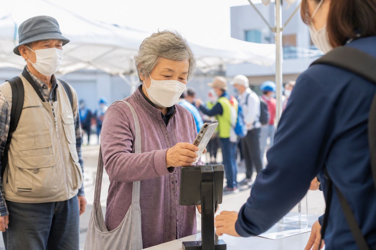 屋外の防災訓練会場でスマホをかざして参加登録する高齢者
