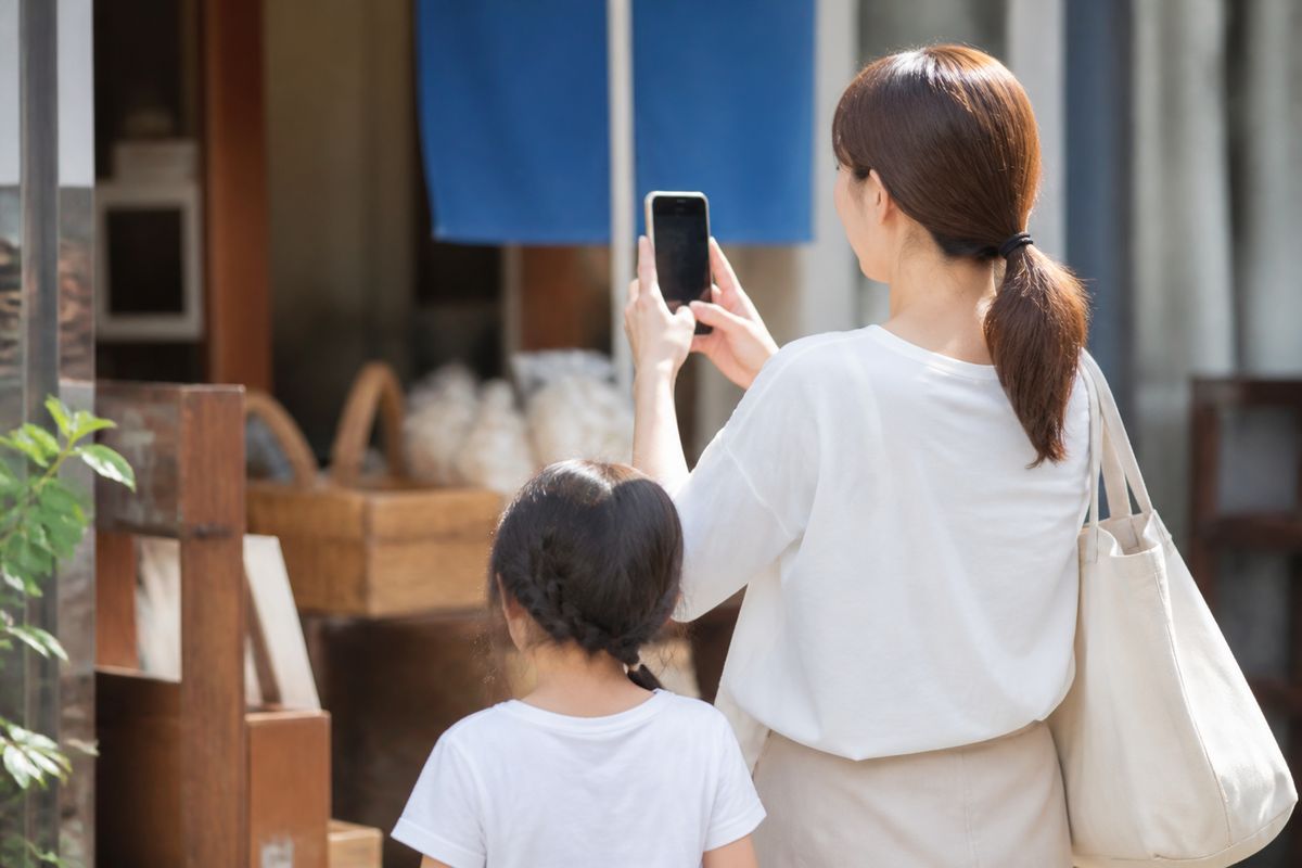 商店街の店先でスマートフォンを掲げてQRコードを読み取る親子の後ろ姿