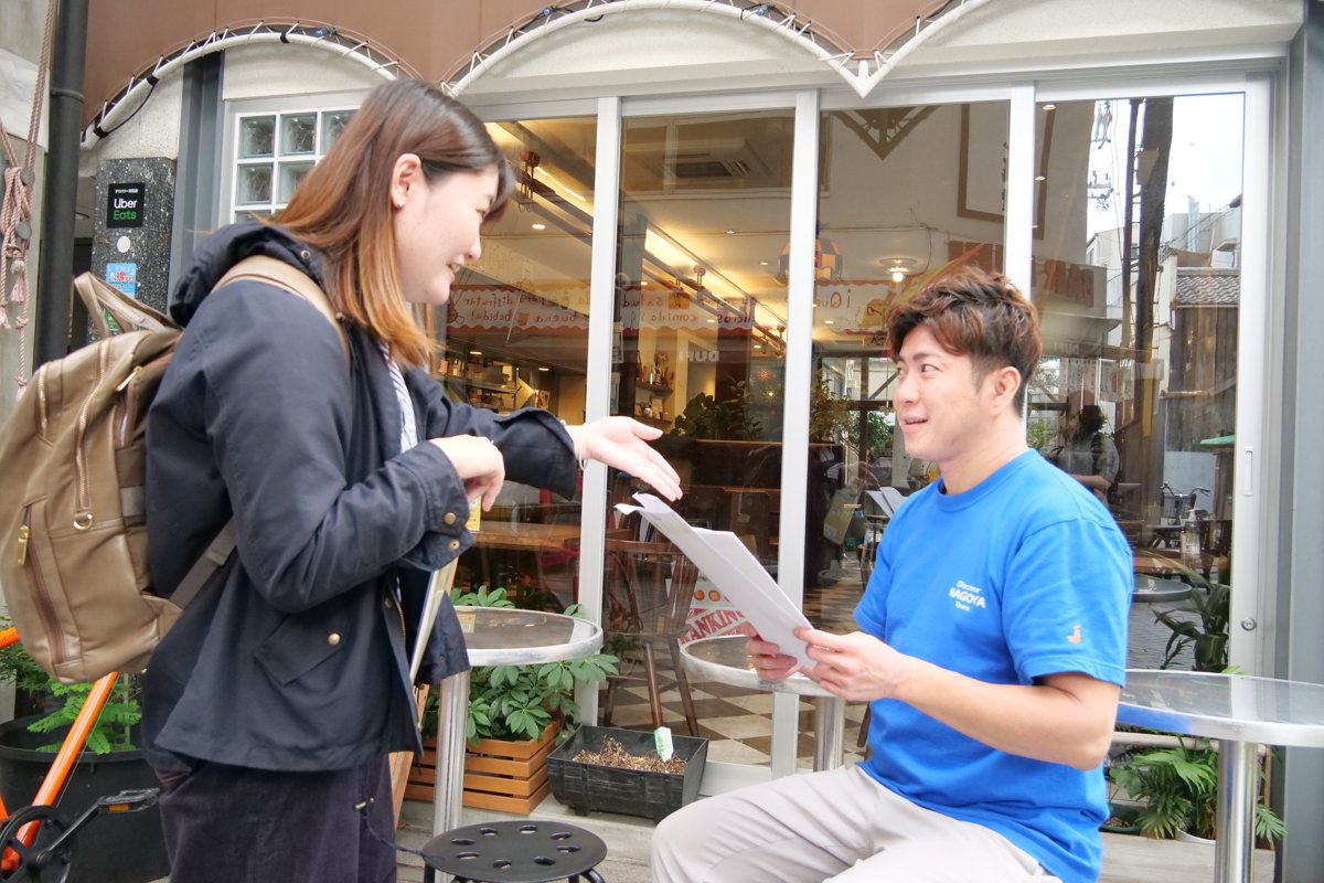商店街の店先でチラシを手に声をかける高木さん