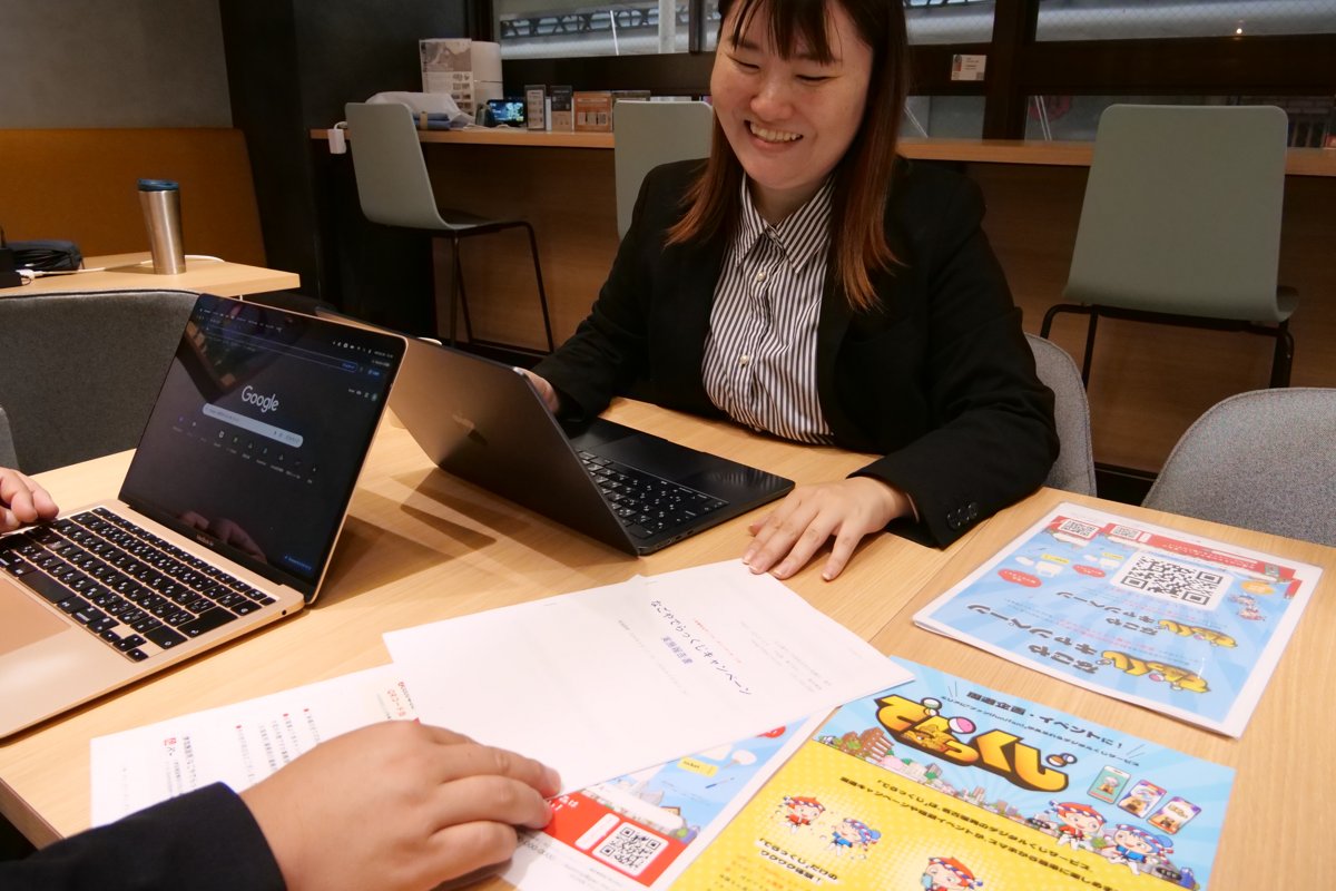 チラシや説明資料を机に広げて、パソコンで作業する高木さん