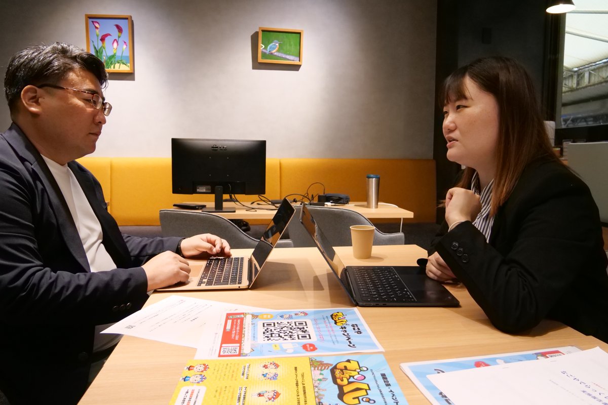 デジタルスタンプラリーのチラシを机に広げて打ち合わせをする高木さん