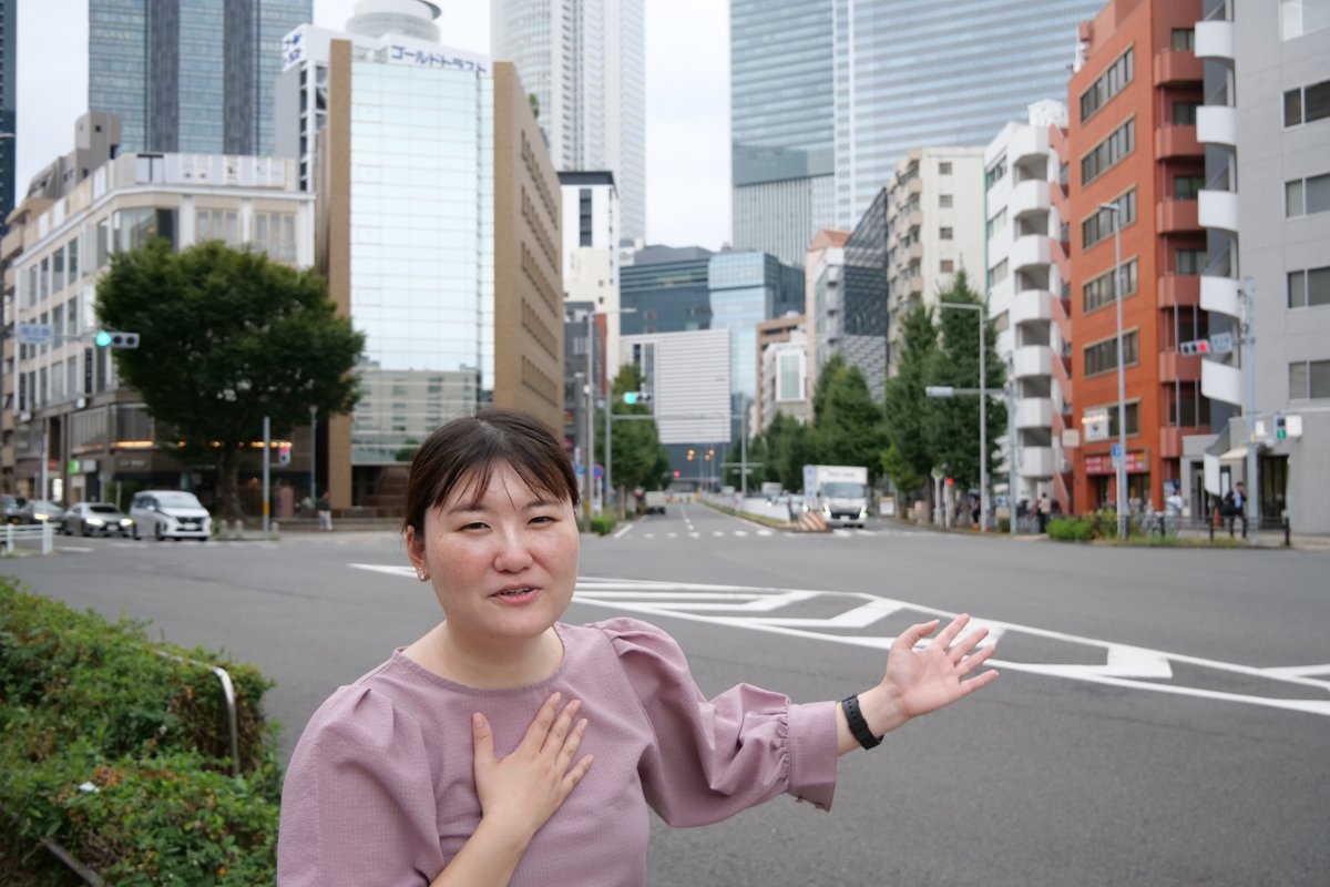 名古屋駅近くの通りで、街なかのスポットを手で示す高木さん