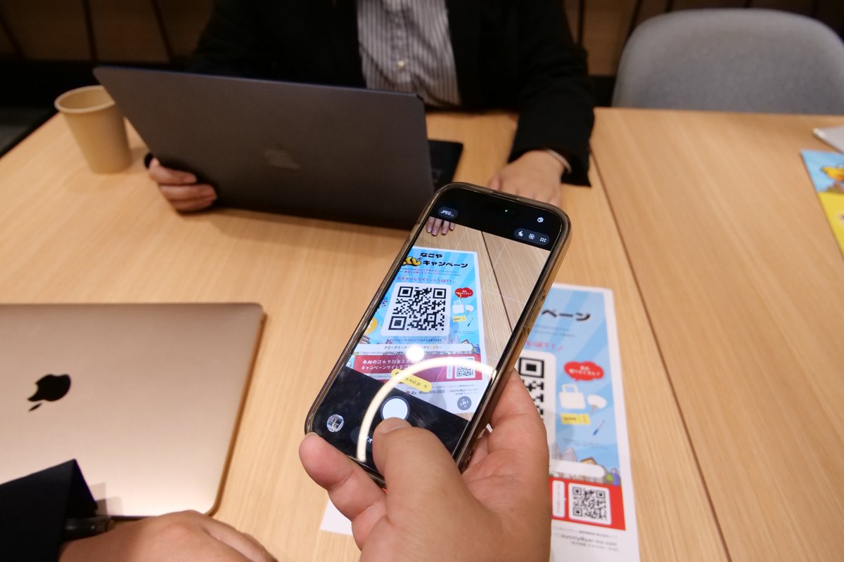 打ち合わせの机で、デジタルスタンプラリーのQRコードをスマホで読み取る様子