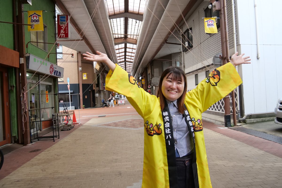 でらっくじのはっぴを着て、円頓寺商店街のアーケードに立つ高木さん
